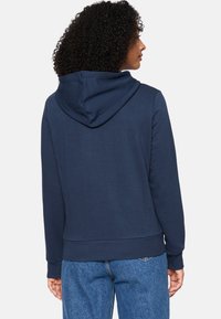 Sudadera azul marino con bolsillo canguro, cordón ajustable, puños acanalados y dobladillo. Tejido suave y texturizado con un corte holgado.