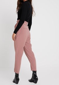 Light pink high-waisted trousers with a loose fit, featuring a smooth texture and side pockets, paired with black ankle boots.