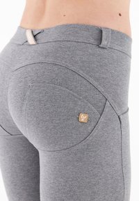 Leggings grigi in tessuto elasticizzato con cuciture curve, un piccolo marchio e una texture liscia. Presentano una vita alta e un design aderente.