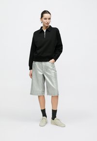 Μαύρο φούτερ με φερμουάρ και κολάρο, σε συνδυασμό με μεταλλικά ασημί σορτς μέχρι το γόνατο. Ολοκληρώνεται με ελαφριά αθλητικά παπούτσια και σκουρόχρωμες κάλτσες.