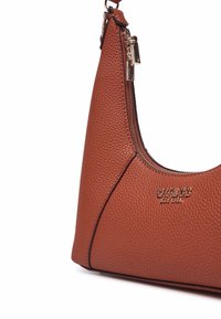 Borsa a tracolla in pelle marrone con una texture a pietra pomice, forma curva, chiusura a zip e dettagli di branding in tonalità dorata.