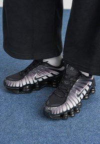 Os sapatos Nike apresentam um upper em malha com um gradiente preto e cinza, detalhes em branco, almofadas da sola arredondadas e um acabamento texturizado.