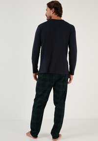Marineblå langærmet skjorte parret med grønne og sorte ternede pyjamabukser. Blødt stof, løs pasform og en afslappet silhuet.