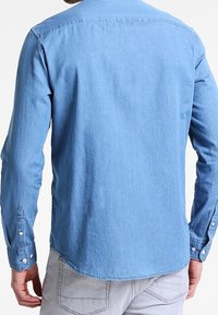 Camicia di jeans azzurro chiaro con maniche lunghe, polsini abbottonati, colletto a punta e orlo curvo. Presenta una texture morbida e un design informale.