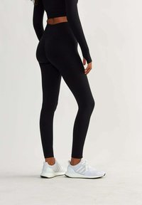 Black leggings with a ribbed texture and high waist, paired with white athletic shoes featuring mesh fabric and lacing details.