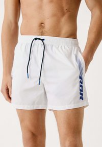 Bañadores blancos con cordón marino y logo "RBR", con rayas diagonales azules en el costado y un corte clásico.
