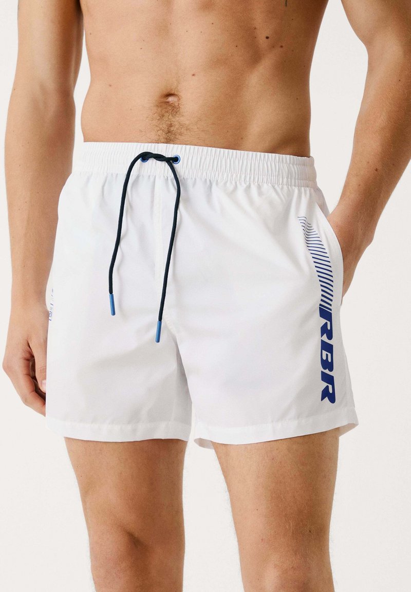 Bañadores blancos con cordón marino y logo "RBR", con rayas diagonales azules en el costado y un corte clásico.