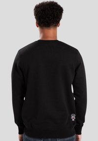 Sudadera negra de corte clásico, con cuello redondo de canalé, mangas largas y un pequeño detalle de logo blanco en la parte baja de la espalda.