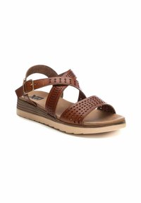 Sandal de cuero marrón con diseño perforado, correa ajustable en el tobillo y suela de cuña baja. Cuenta con una plantilla acolchada para mayor comodidad.
