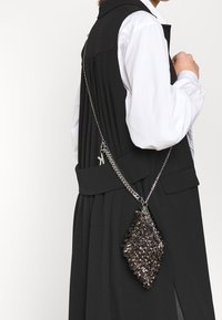 Czarna torebka na ramię z teksturowymi ozdobami, metalowym łańcuszkiem, w kształcie diamentu oraz błyszczącymi akcentami ze stali.
