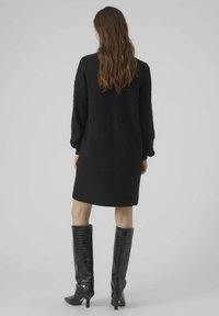 Abito nero intrecciato con un motivo testurizzato, maniche lunghe e una vestibilità rilassata, abbinato a stivali neri in vernice al ginocchio.