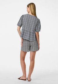 Top a righe bianche e nere con maniche a sbuffo, abbinato a pantaloni corti coordinati. Tessuto leggero, vestibilità rilassata e design peplum.