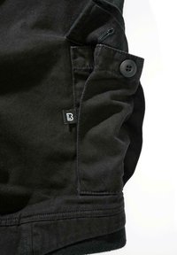 Juodi medvilniniai šortai su šonine kišenėle su saga, matomomis siūlėmis ir mažu prekės ženklo etiketės audeklo paviršiuje.