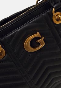 Schwarze gesteppte Handtasche mit goldfarbenen Beschlägen, ausgestattet mit einem auffälligen, geprägten Logo und doppelten Metallringen zur Befestigung des Riemens.