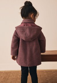 Manteau à carreaux violets et roses avec une capuche, doté d'un col lisse et de manches longues, porté avec un pantalon noir, vu de dos.