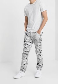 Grå t-shirt i kombination med vita byxor med ett texturerat månlandskapmönster. Outfitten fulländas med vita sneakers.