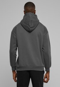 Grå fleecehoodie med en stor, afslappet hætte, ribbede manchetter og hurtig, glidende struktur uden synlig branding.