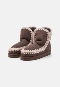 Stivaletti alla caviglia in suede marrone con bordatura intrecciata beige, fodera morbida e suola piatta e testurizzata per una migliore aderenza.