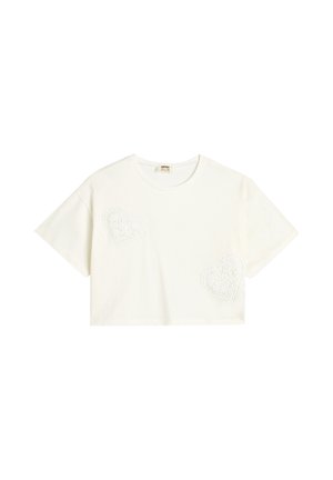 T-shirt court blanc en coton, ornée de deux motifs de cœur en dentelle texturée à l'avant. Manches courtes et col rond.