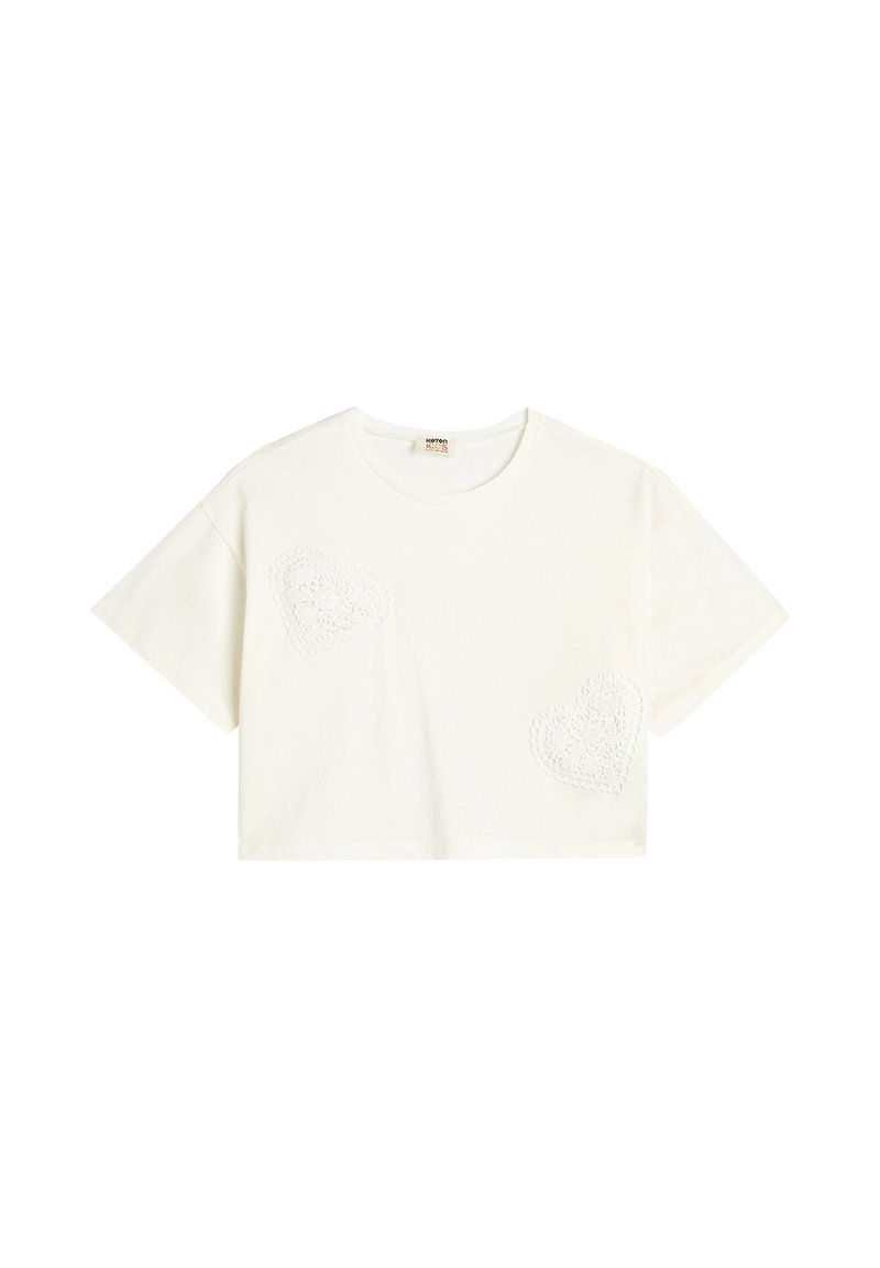Camiseta corta blanca de algodón, con dos diseños de corazones texturizados de encaje en la parte delantera. Mangas cortas y cuello redondo.