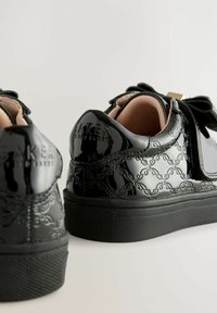 Sneakers in pelle verniciata nera con motivo in rilievo, dotati di punta arrotondata, suola spessa nera e fiocco decorativo sulla parte anteriore.