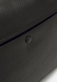 Borsa in pelle nera con superficie texture, dotata di chiusura a scatto nera e dettagli di cucitura discreti lungo il bordo.