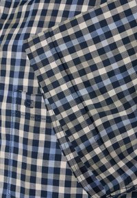 Blauw en grijs geruit stof met een klein pocketdetail. Lichtgewicht textuur, met variërende maten van ruitjes en gestikte naden.