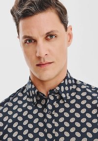 Granatowa koszula zapinana na guziki, ozdobiona kwiatowym wzorem z jasnymi stokrotkami, z kołnierzykiem oraz teksturowanym materiałem o gładkim wykończeniu.