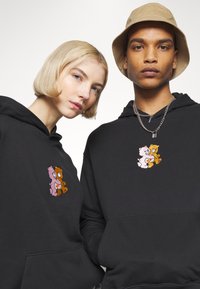 Black hoodies feature a cartoon design of two bears, one pink and one brown, embroidered on the chest. Soft fabric, pullover style, and attached hood.