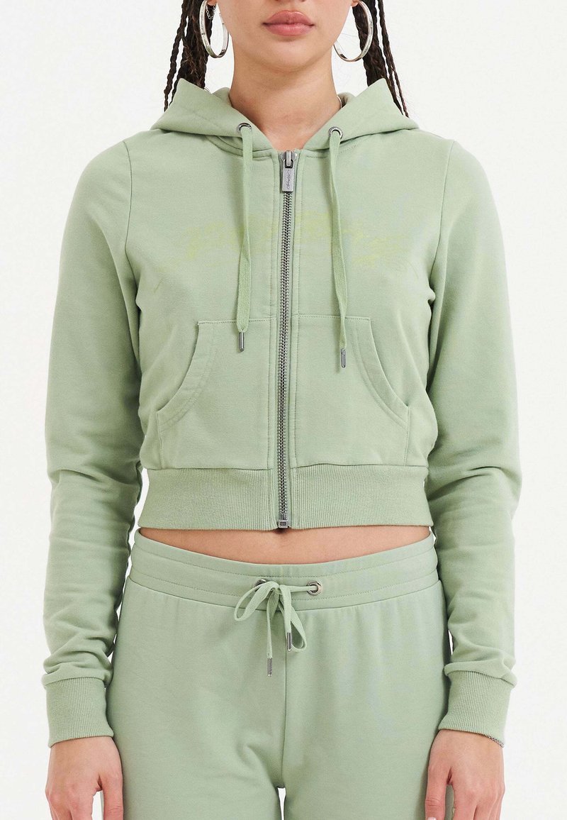 Lichtgroene crop hoodie met rits, voorzien van twee voorzakken en ribgebreide manchetten. Gecombineerd met bijpassende joggers.