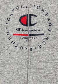 Sudadera con cremallera gris hecha de tela suave, que presenta un logotipo circular en marino y rojo, con un gran texto que dice "Champion Rochester NY".