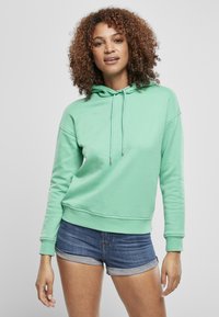 Felpa verde menta in morbido tessuto, con cappuccio regolabile, polsini a costine e una vestibilità rilassata, abbinata a pantaloni corti di jeans.