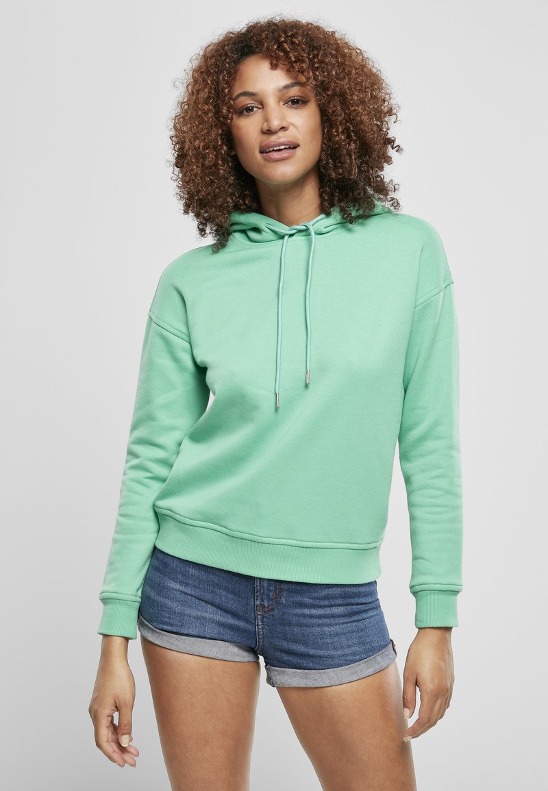 Felpa verde menta in morbido tessuto, con cappuccio regolabile, polsini a costine e una vestibilità rilassata, abbinata a pantaloni corti di jeans.