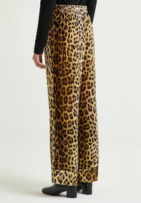 Pantaloni a zampa larga con stampa leopardata in tessuto morbido e strutturato, con cintura elastica e orlo rifinito, abbinati a una maglietta nera e scarpe con tacco.