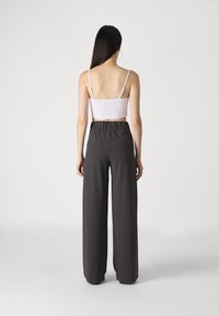 Pantalones grises de pierna ancha con cintura elástica, combinados con una blusa blanca de tirantes finos ajustada. Textura suave, diseño minimalista.