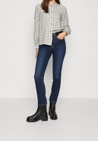 Chemise à carreaux blanche et noire, jean skinny bleu et bottes noires en cuir jusqu'aux genoux avec semelles épaisses et détails de boucles.