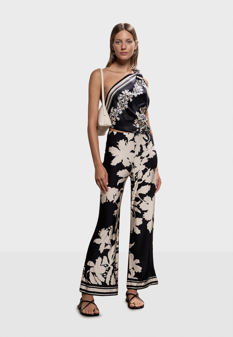 Ensemble en satin noir à motifs floraux comprenant un haut asymétrique avec un nœud et un pantalon à jambes larges. Orné de motifs floraux crème et de finitions assorties.