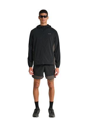 Mand iført sort lynlåstrøje med hætte, matchende shorts, sorte sokker, sneakers og solbriller, stående og vendt fremad.