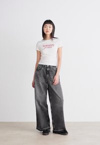 Bílá bavlněná tričko s červeným logem "tommy jeans"; kombinované se šedými širokými džínsy a černými botami. Jednoduchý a neformální design, minimální textura.