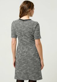 Abito grigio a maniche corte con un motivo a quadri testurizzato, dalla silhouette aderente e con bordi neri sul colletto.