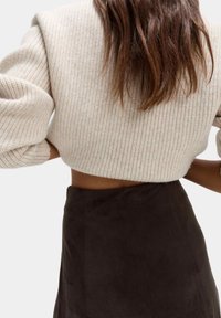 Maglione beige corto e testurizzato con motivo a coste, abbinato a una gonna in suede marrone scuro. Mostra la vista posteriore e i dettagli delle braccia.