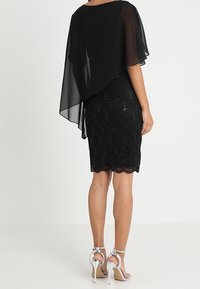 Svart paljettklänning med ett genomskinligt svart mantelöverdrag, vågig nederkant och silverhöga sandaler. Slät textur och figurnära passform.