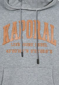 Felpa grigia con cappuccio e coulisse regolabile, con testo arancione "KAPORAL" e "LIVE WORK REBEL" e coordinate geografiche stampate sul davanti.