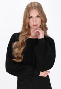 Zwarte gebreide trui met een brede halslijn en poffende lange mouwen. Fijne textuur met geribde boorden en zoom, gestyled met een op maat gemaakte zwarte broek.