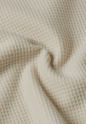 Beige wafelkatoen stof met zachte plooien en een gestructureerd ruitpatroon.