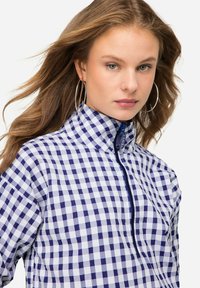 Camicia colletto in blu e bianco con motivo a scacchi; presenta una chiusura frontale a mezza zip e una finitura in tessuto testurizzato.