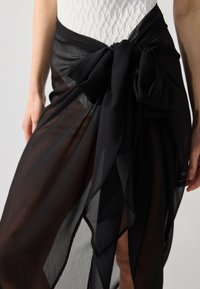 Jupe en tissu transparent noir avec un grand nœud à la taille, au design fluide et à la texture légère.