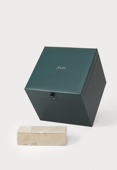 Caja de regalo cuadrada verde con letras doradas "JIA JIA" y una pequeña caja de mármol beige con textura suave, colocadas una al lado de la otra.