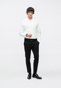 Biela dlhá košeľa na gombíky s dlhým rukávom, čierne spoločenské nohavice, čierne topánky, slim fit, s malým logom na košeli. Jednoduchý a moderný dizajn.