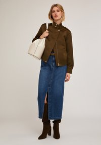 Jachetă verde măslinie cu fermoar, cu guler înalt, asociată cu o fustă din denim cu o deschidere frontală și bots de piele întoarsă, până la genunchi, de culoare maro.